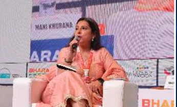 A woman in a peach outfit speaking during a Day 1 conference session